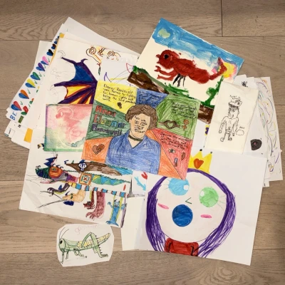 A pile of kids' drawings and paintings spread across a wooden floor